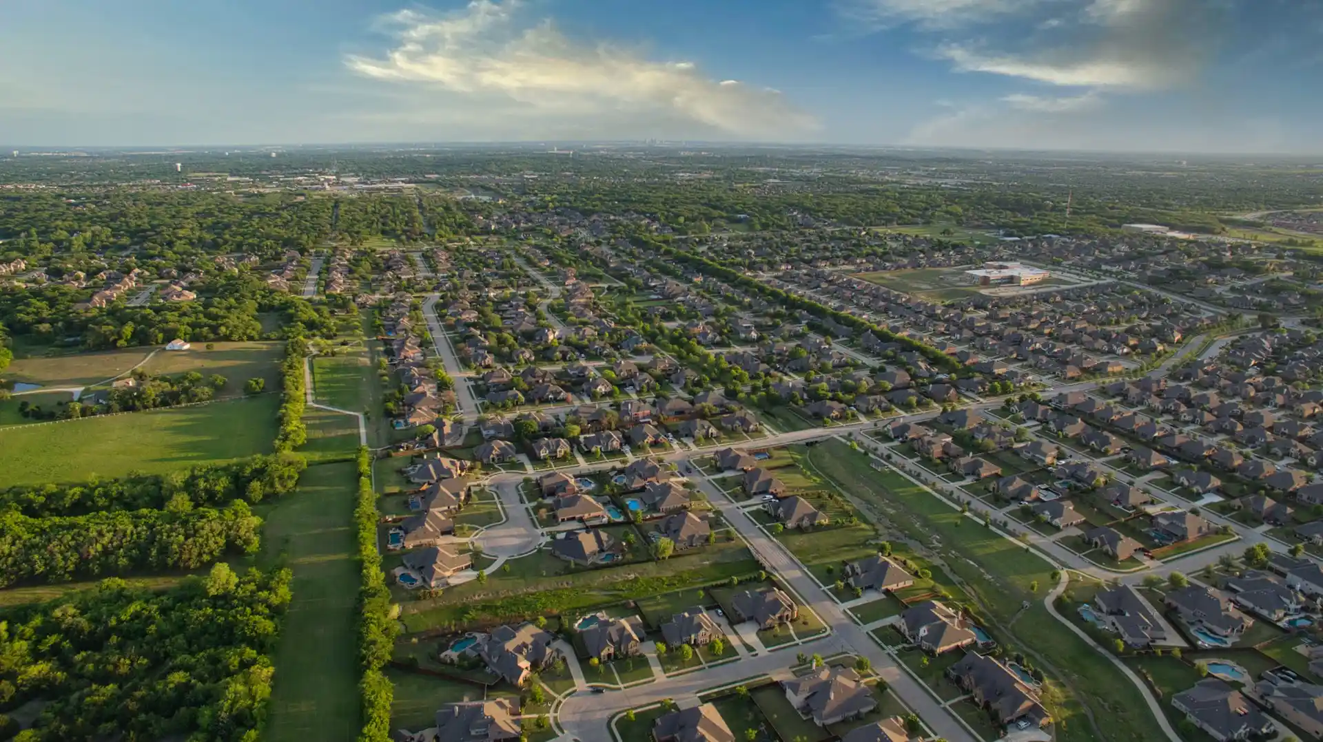 An aerial view of a sprawling suburban residential area bordering green fields, showing a developed community that real estate revitalizes communities.
