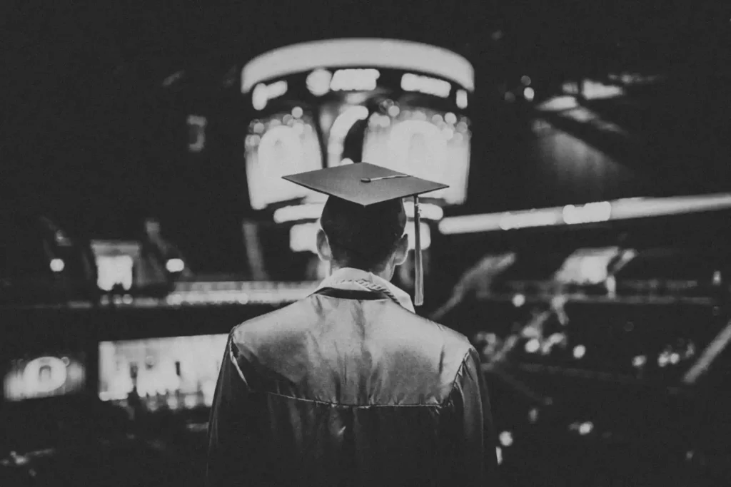 A graduate in a cap and gown looking towards a bright scoreboard in a stadium, symbolizing the future opportunities created when you start a scholarship fund.