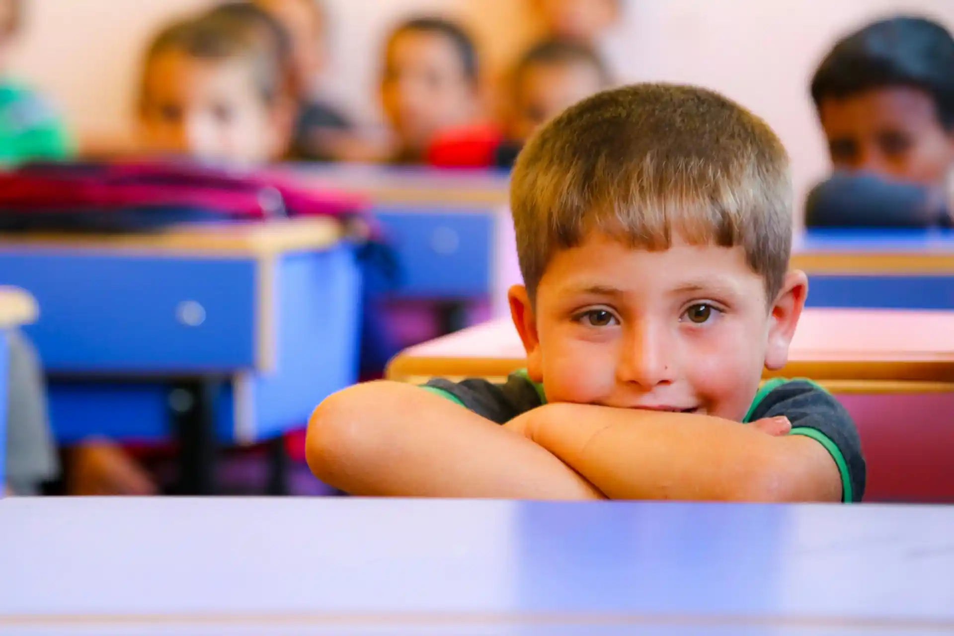 A young boy smiling confidently from his desk in a classroom, representing the bright future fostered by education philanthropy.